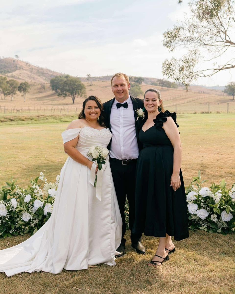 Simone with a bride and groom in front of rolling Queensland hills